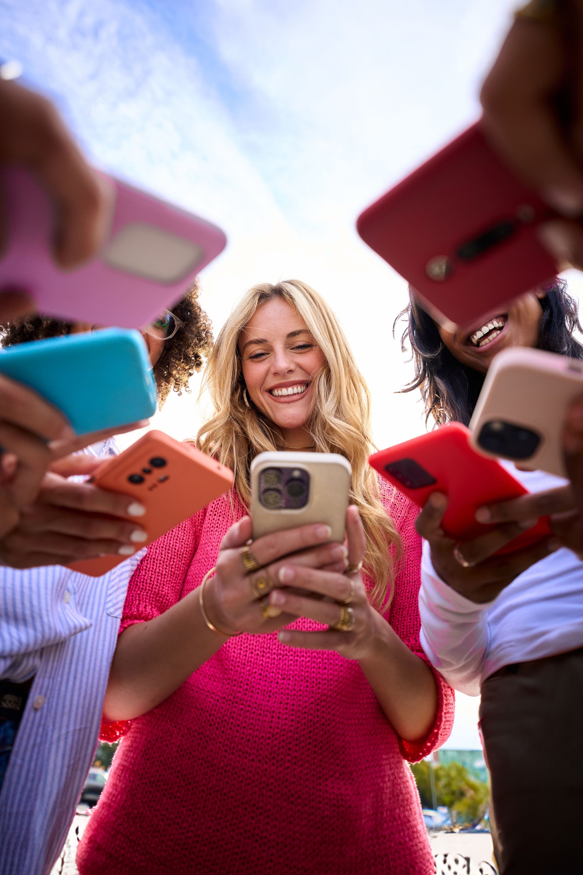 Low angle of happy gen z blonde woman smiling standing in only girls circle looking at cell outdoor.